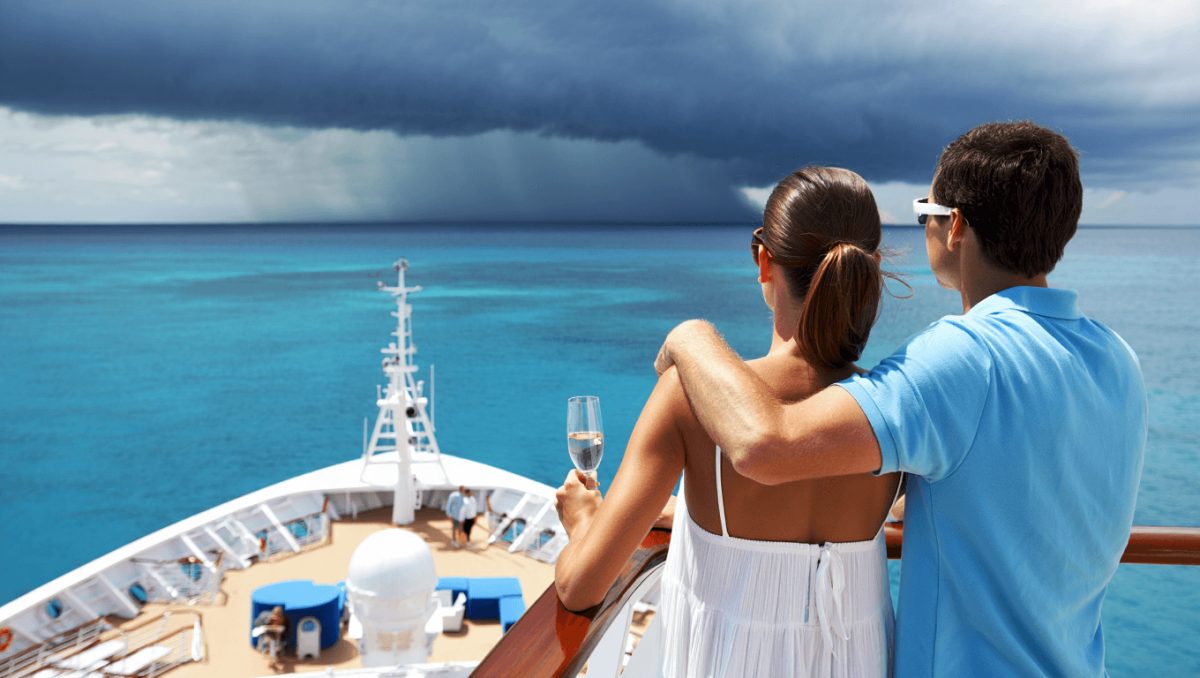 Side of a cruise ship with trees and ocean in background