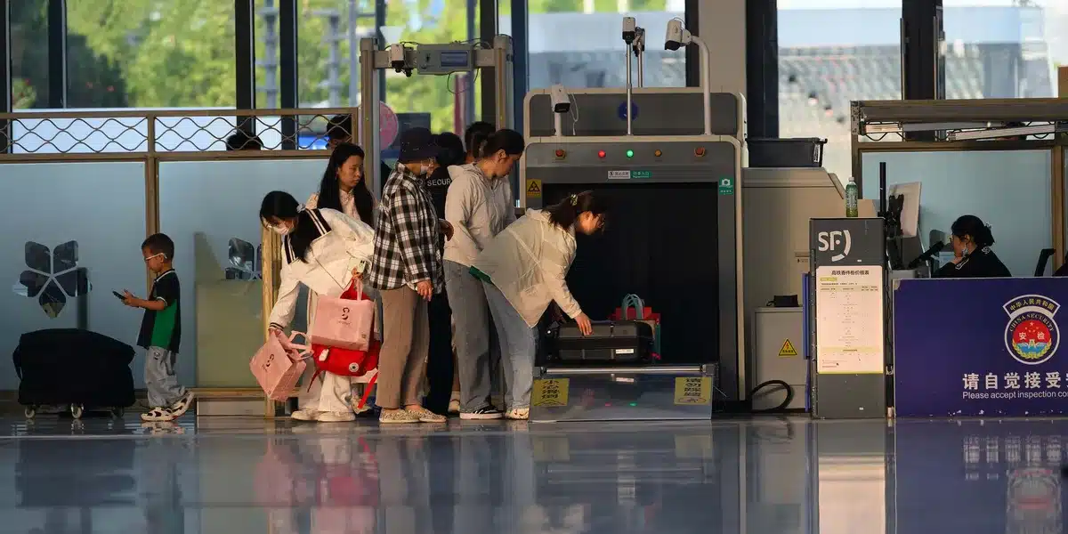 Passengers waiting in a security queue at an airport with carry-on luggage