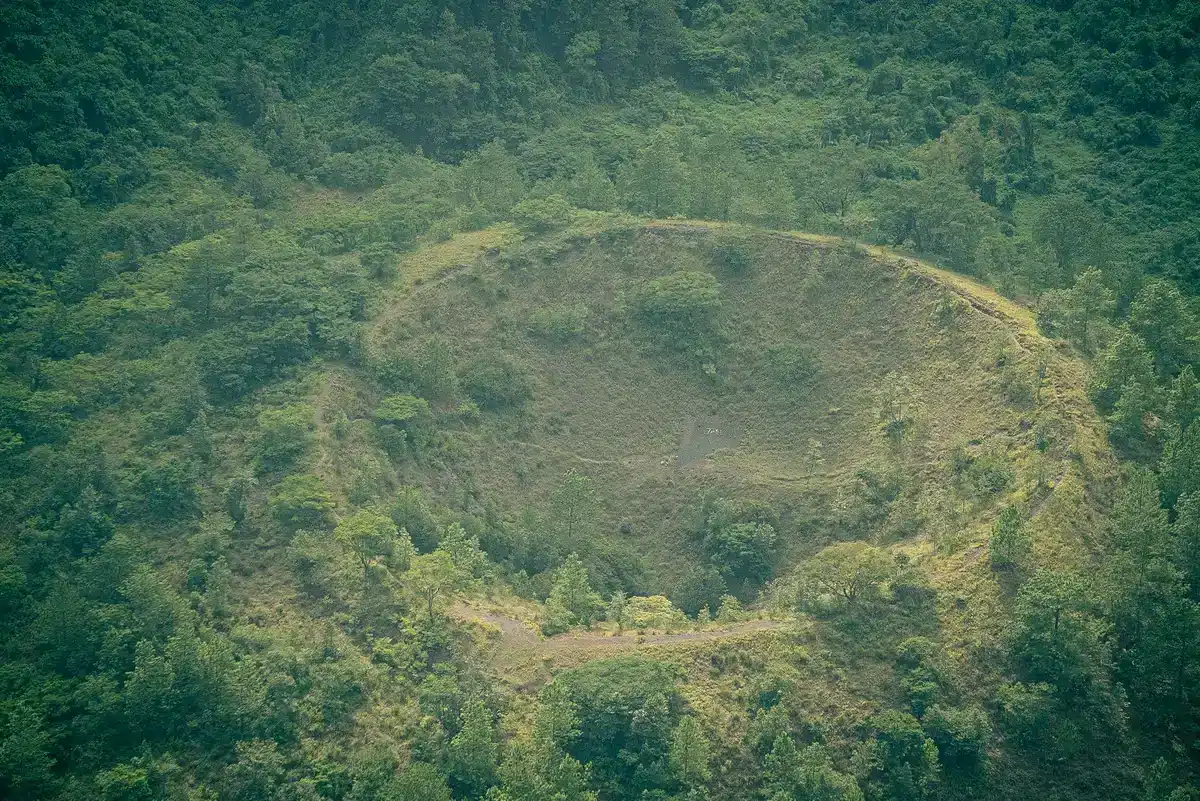 Hiker on a mountain trail with steaming volcanic crater and dense forest