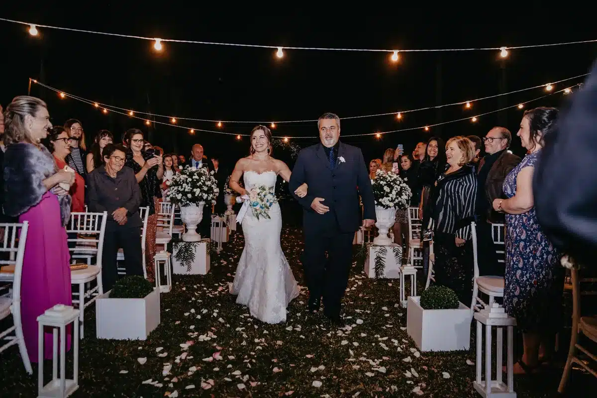 Bride walking alone down an outdoor aisle toward groom on family estate