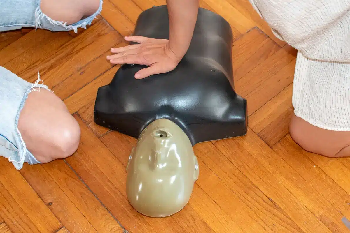 Instructor guiding a participant through CPR technique on a training dummy.