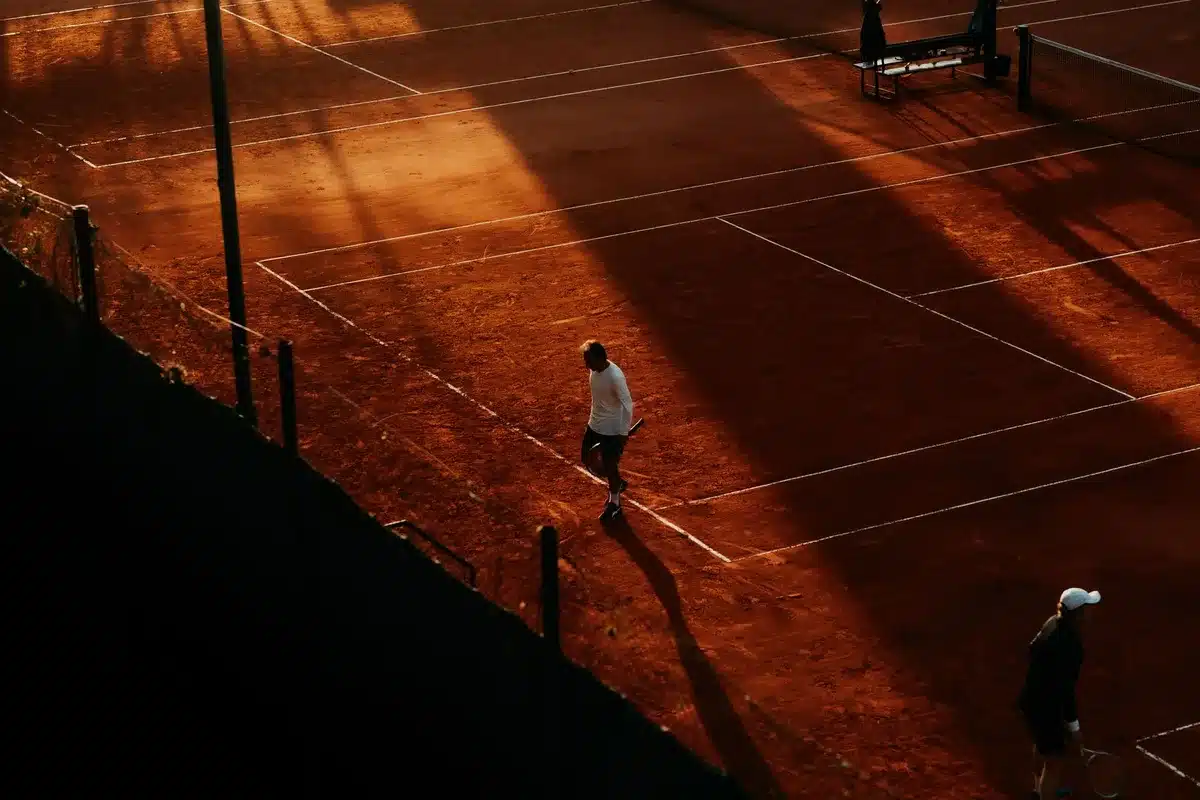 Tennis player executing a serve on an outdoor court at sunrise, demonstrating athletic form and focus.