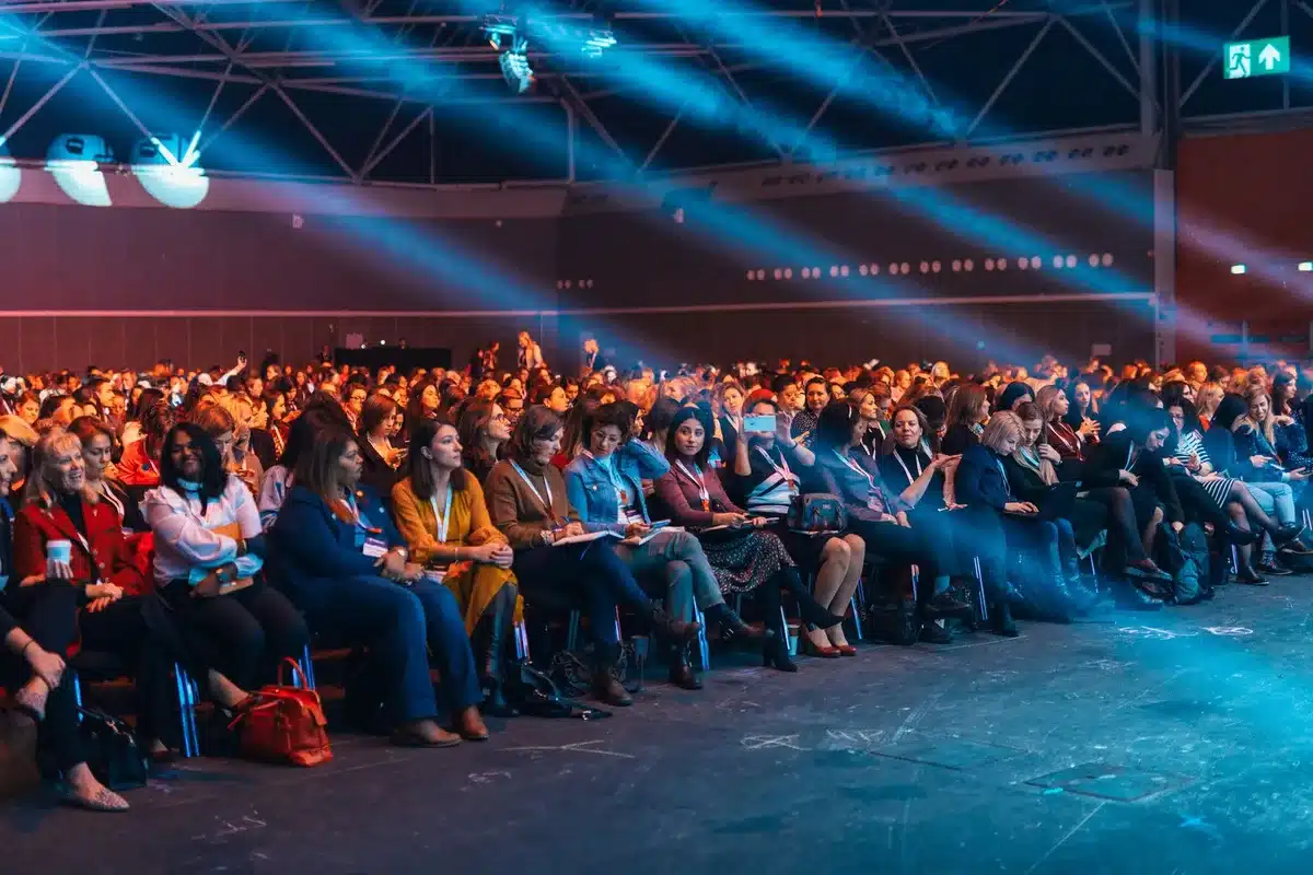 A crowded convention center audience watching a panel discussion on stage.