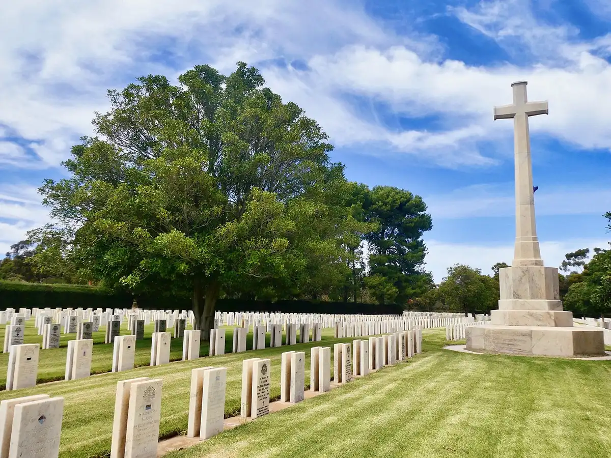 Ornate cemetery memorial grounds with fresh flowers at a headstone and a silhouetted mourner