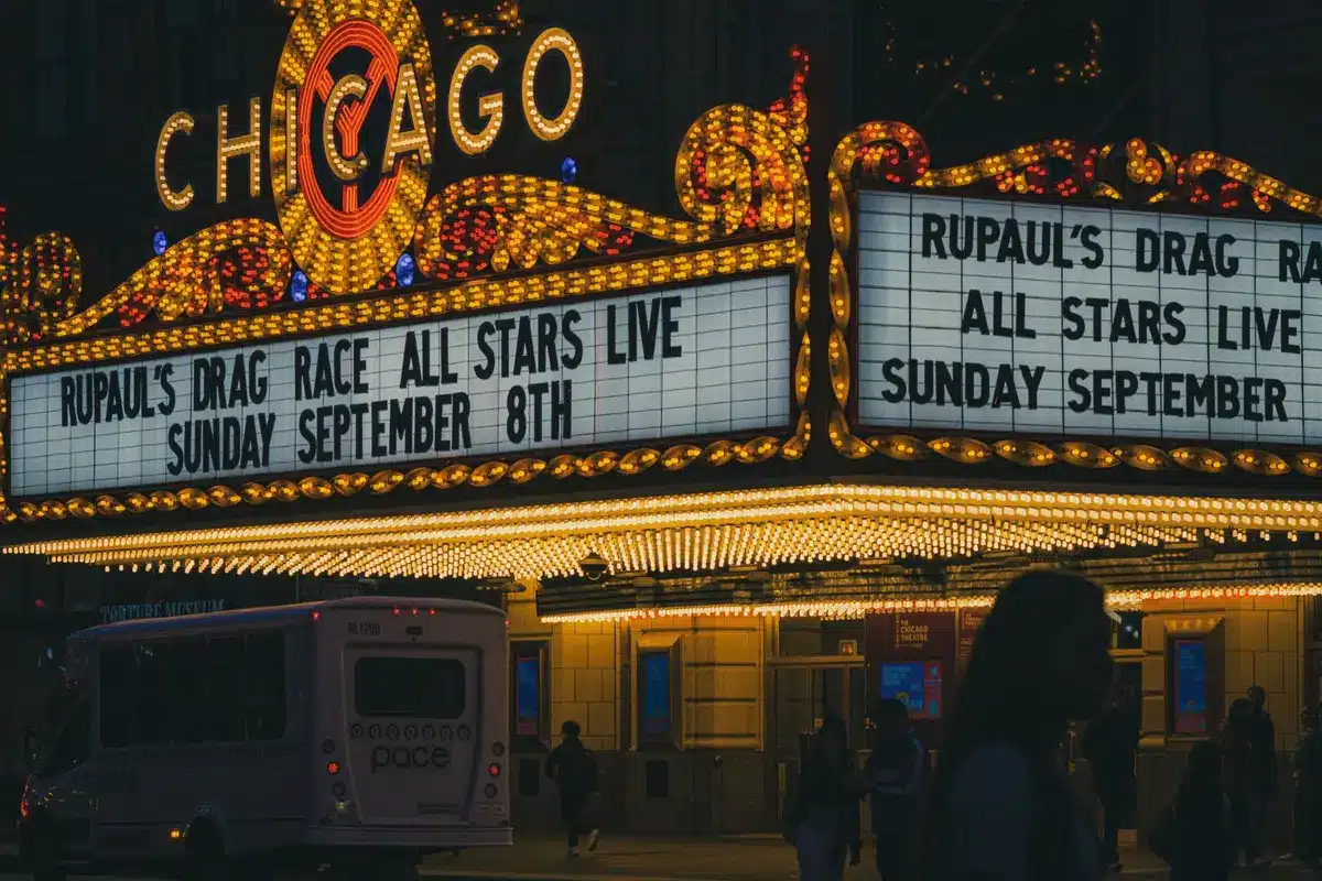 Broadway theatre marquee lit at dusk with silhouettes of audience members entering through doors