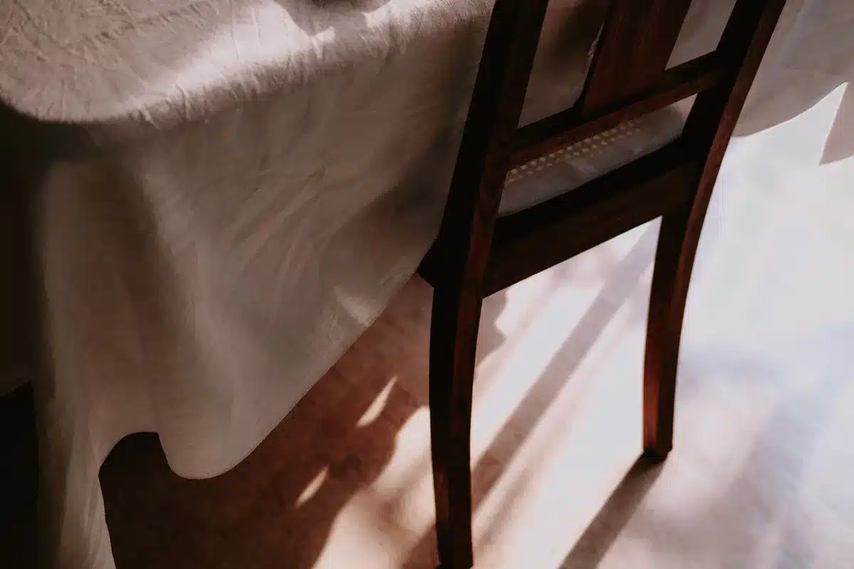 An empty chair by a window with soft light and a framed photograph of a couple nearby