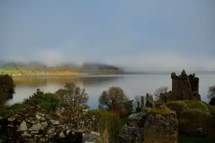 Misty Highland valley with golden autumn trees and a still loch reflecting peaks in morning fog