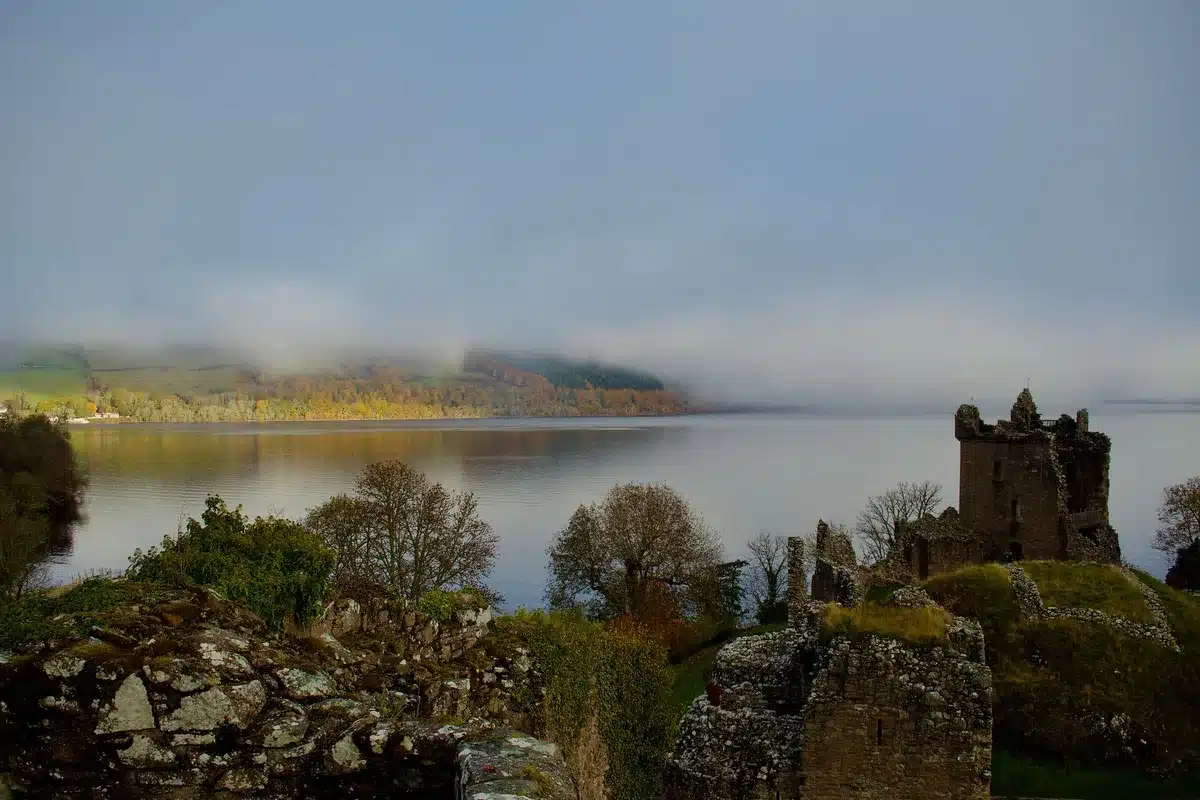 Misty Highland valley with golden autumn trees and a still loch reflecting peaks in morning fog