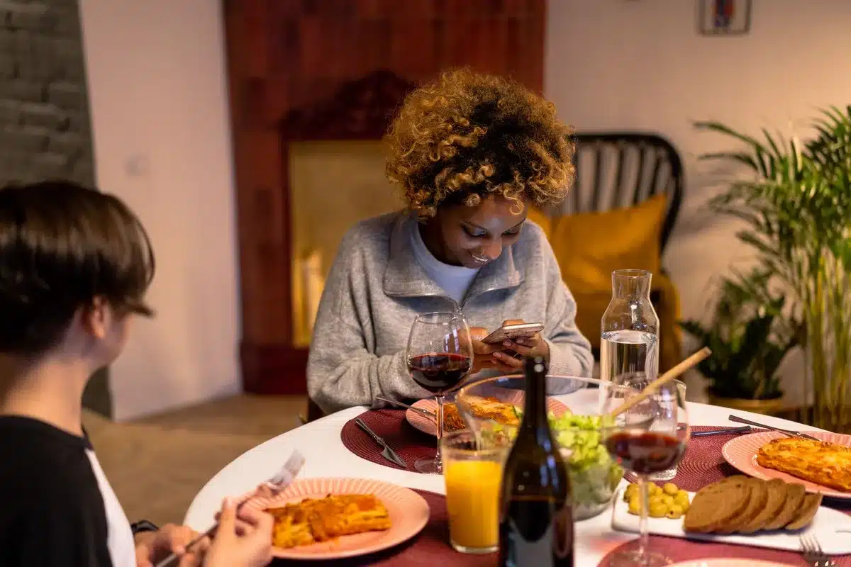 Smartphone displaying a social media post on a table with wine glasses and place settings in the background