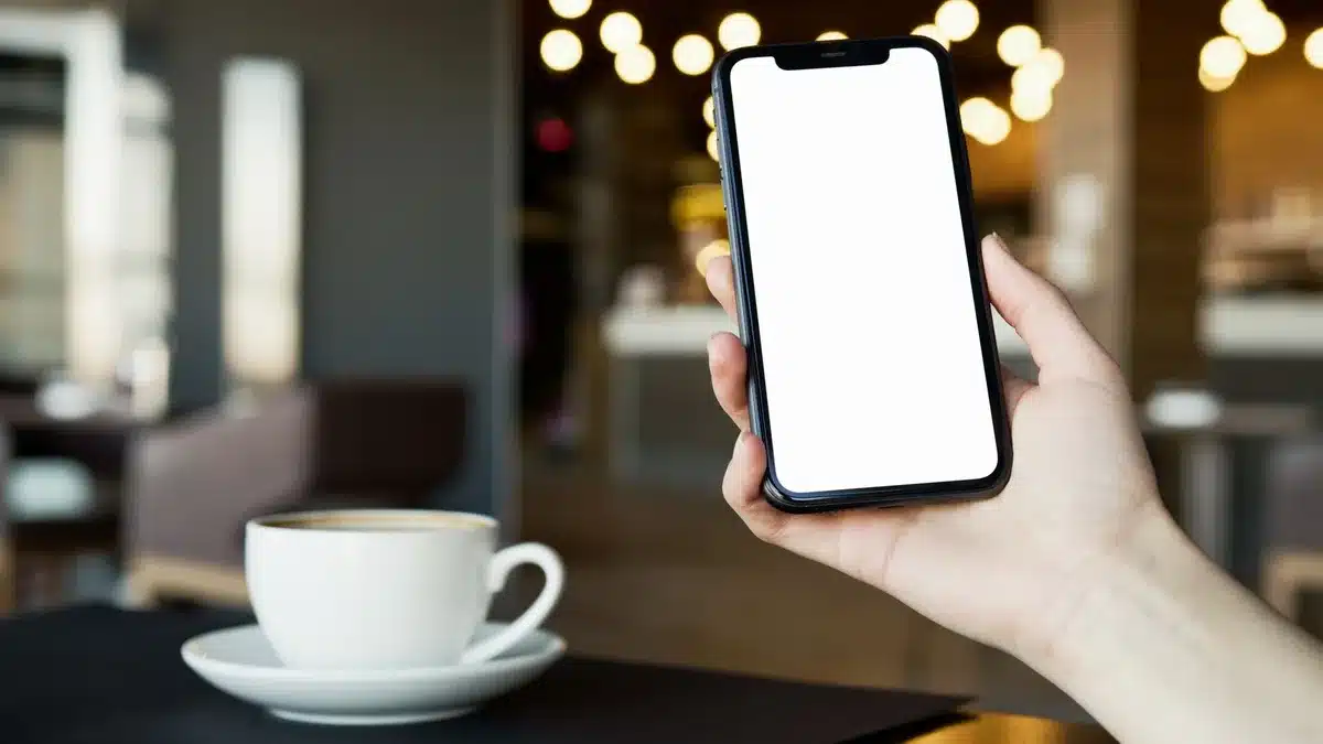 Customer holding a coffee cup next to a smartphone showing a rewards app at a café counter