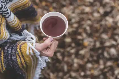Hands holding a warm pumpkin spice latte with steam rising, autumn backdrop