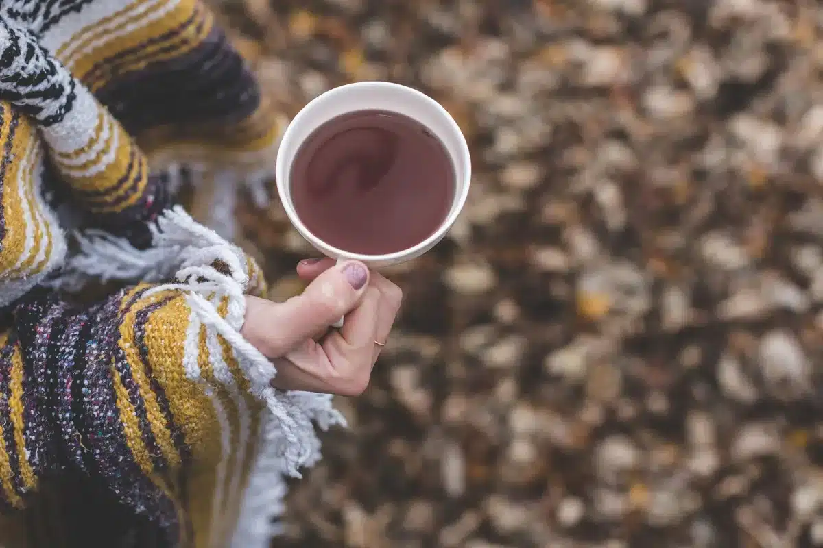 Hands holding a warm pumpkin spice latte with steam rising, autumn backdrop