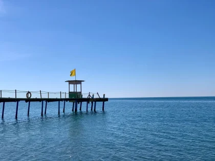 Traveler strolling through a peaceful beachside plaza with calm waters and clear skies in the distance.