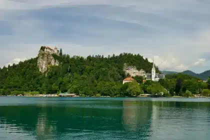Scenic alpine lake with forested slopes and distant mountains, small island with church in center
