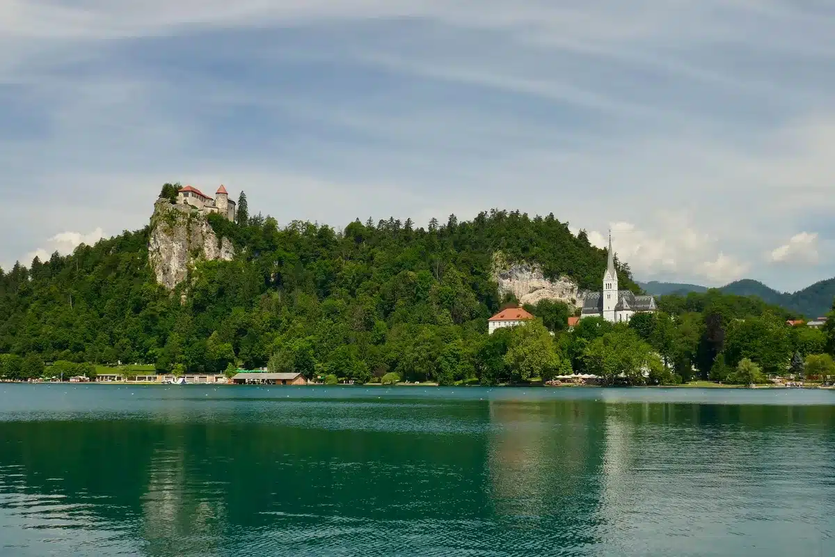 Scenic alpine lake with forested slopes and distant mountains, small island with church in center