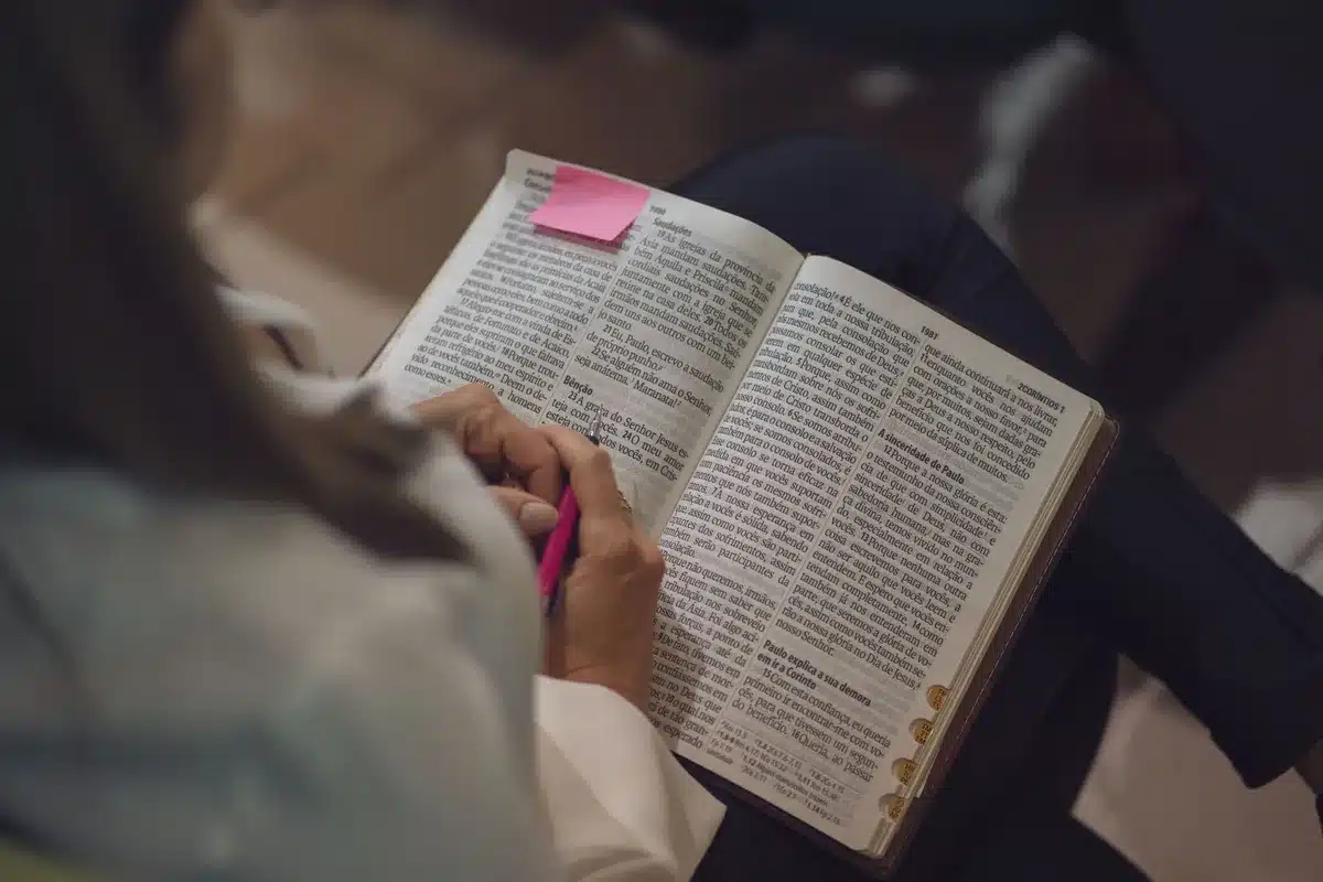 Hands holding an open Bible with candlelit religious setting in background