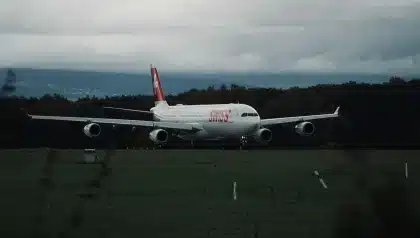 A modern commercial narrowbody jet taxiing on an airport runway at sunrise with distant city skyline.