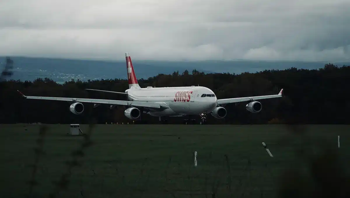 A modern commercial narrowbody jet taxiing on an airport runway at sunrise with distant city skyline.