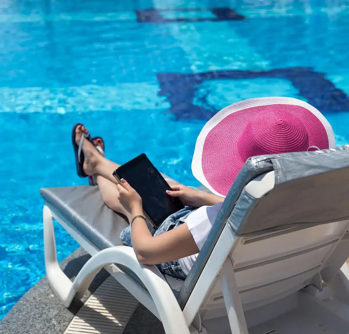 Woman sitting by a pool posting a video on her phone with a small dog nearby