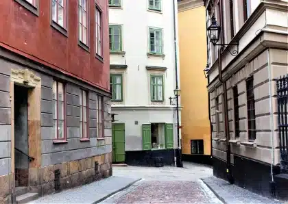 Sunlit narrow stone alley leading to honey-colored medieval walls and a small boat offshore