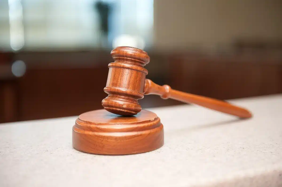 Wheelchair in a courtroom near a counsel table with legal folders and a judge's bench blurred