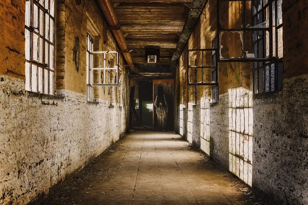 Dimly lit historic hotel corridor with antique carpet and an armchair near a stairwell