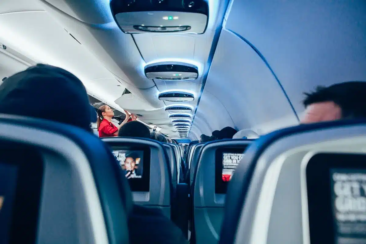 Airplane cabin interior showing passenger seating and flight attendants in the aisle