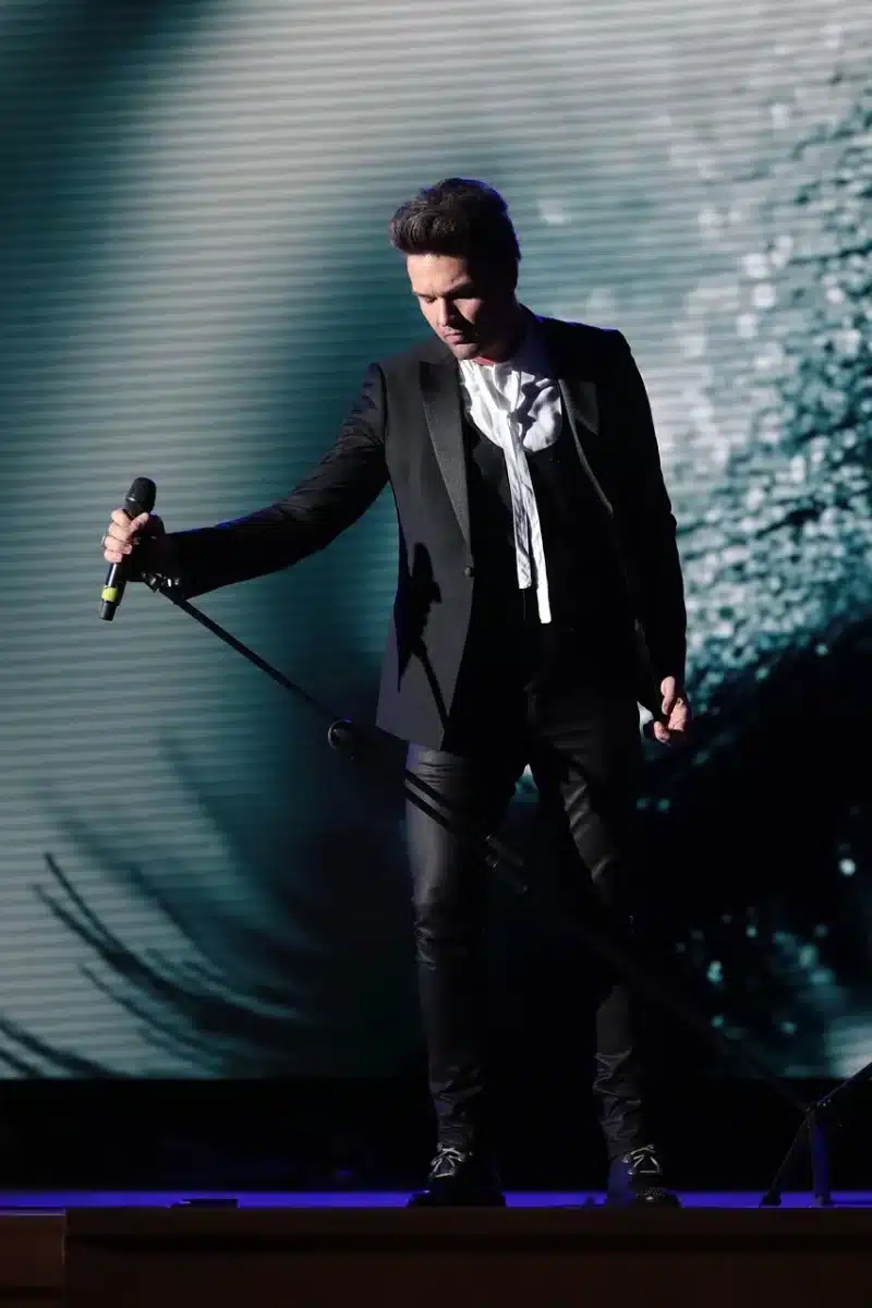 Singer performing on stage at a private fundraiser with soft audience silhouettes