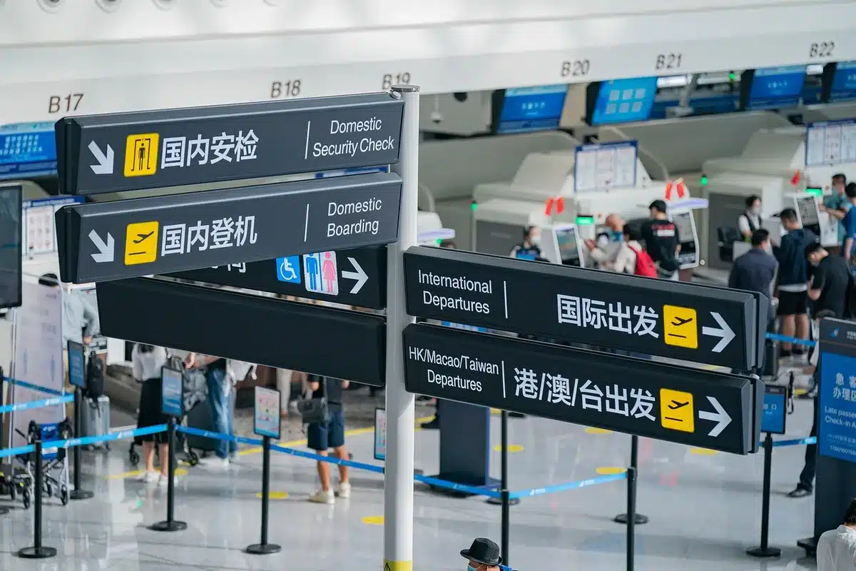 Silhouetted passengers at a gate with a delayed flight display and maintenance cart