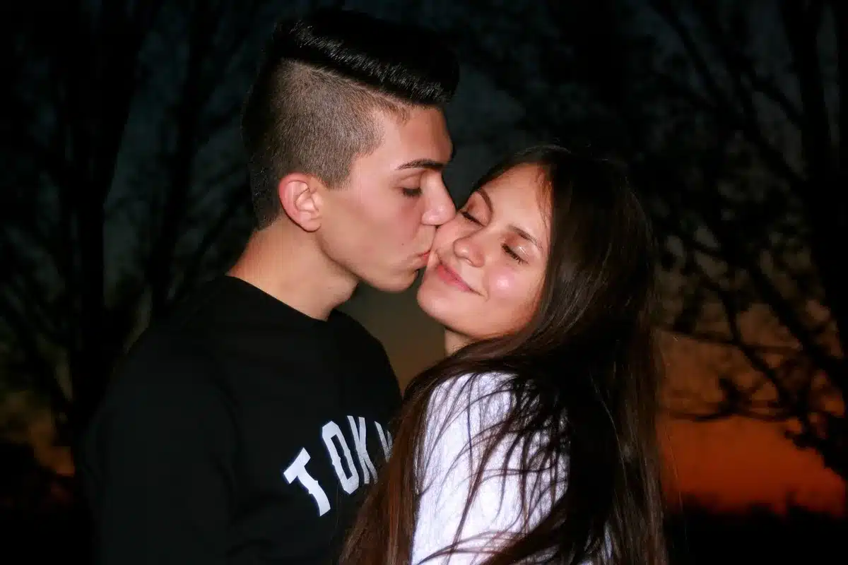 Couple at a red carpet event, evening lights and photographers visible in the background
