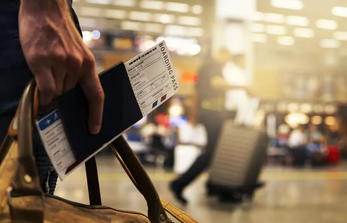 Passengers queuing at an airport gate with flight boards showing departures