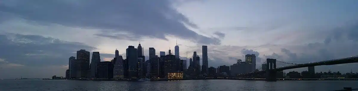 Two anonymous figures walking across the Williamsburg Bridge at dusk with Brooklyn skyline