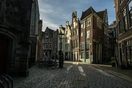 Cobblestone lane with brick shopfronts and a small bakery near a river
