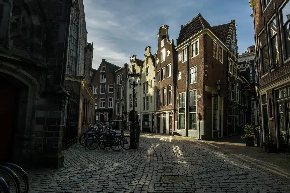 Cobblestone lane with brick shopfronts and a small bakery near a river