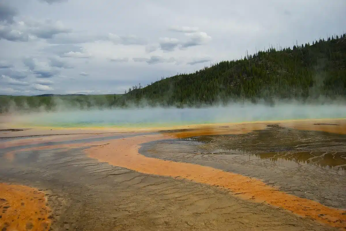 Steam rising from outdoor thermal pools near a riverbank with anonymous visitors