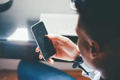 Silhouetted figure holding smartphone displaying fragmented text and political imagery on screen