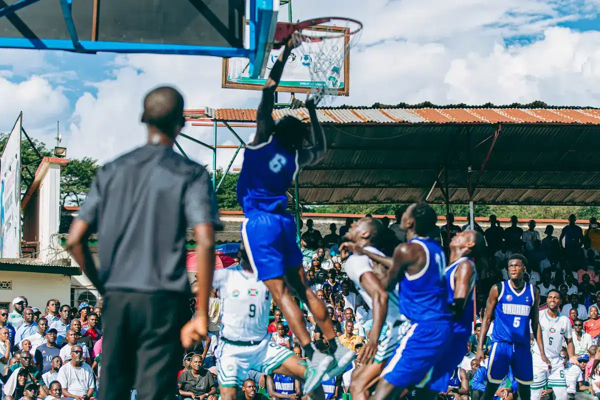 Silhouetted players fighting for a rebound under a hoop at an indoor arena