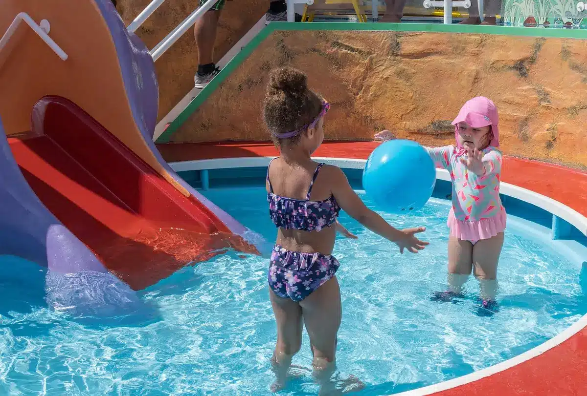 An instructor kneeling by a poolside teaching young children basic swim skills