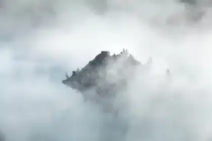 Misty loch shore, distant ruined stone castle and rugged hills under overcast sky