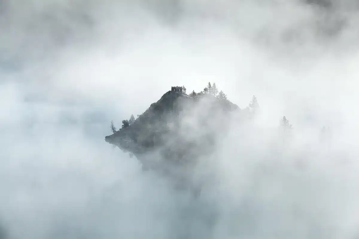 Misty loch shore, distant ruined stone castle and rugged hills under overcast sky