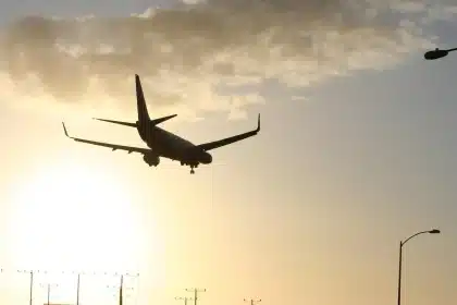 Two silhouettes laughing by an airport arrival board with a suitcase and a generic helmet